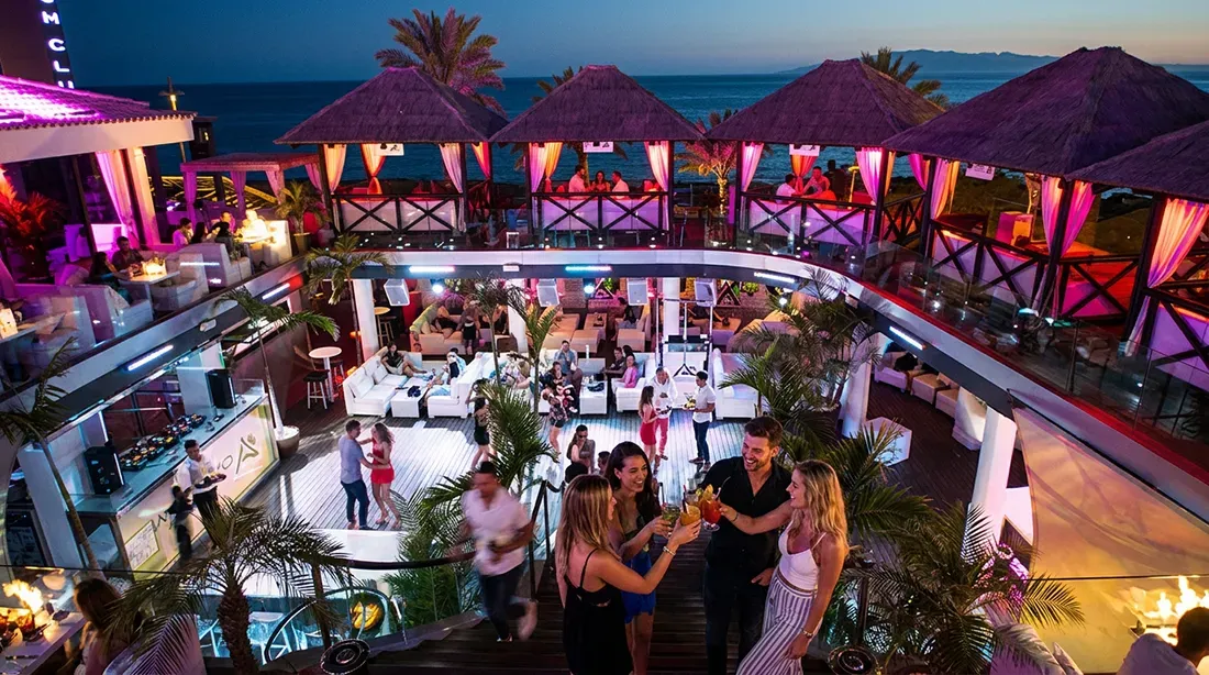 Guests dancing and socializing on illuminated deck with beach club backdrop at night