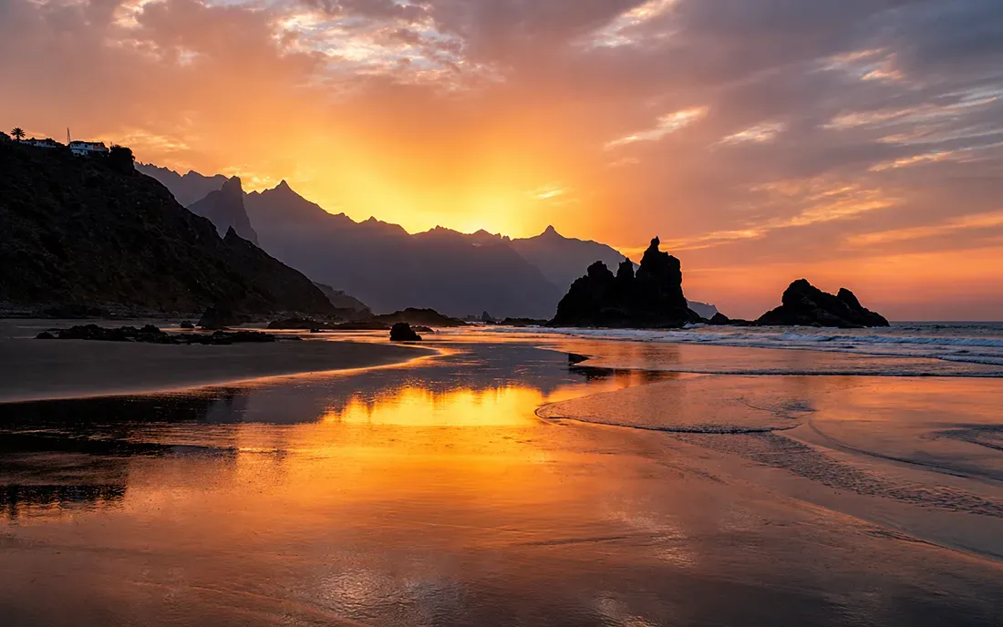 Dramatic sunset over rocky beach with golden sky reflecting on wet sand