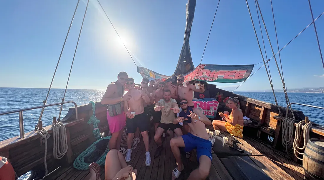 Large group of guests celebrating on wooden sailing boat deck with sails up