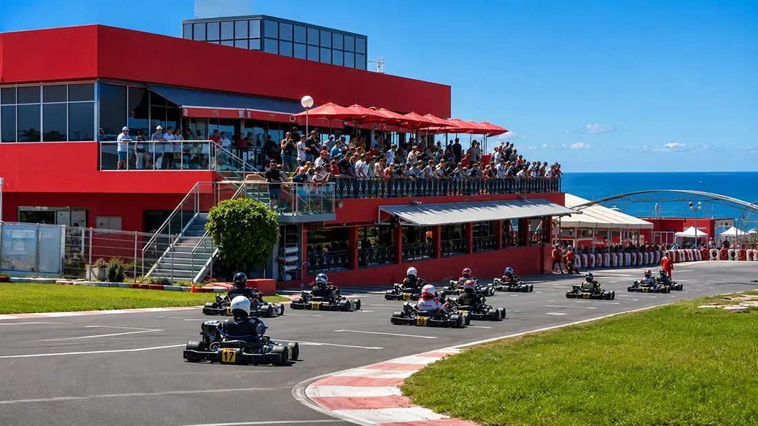 Go-kart race on coastal track with red grandstand and ocean backdrop