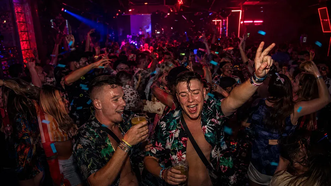 Young men dancing and celebrating in crowded nightclub with neon lighting