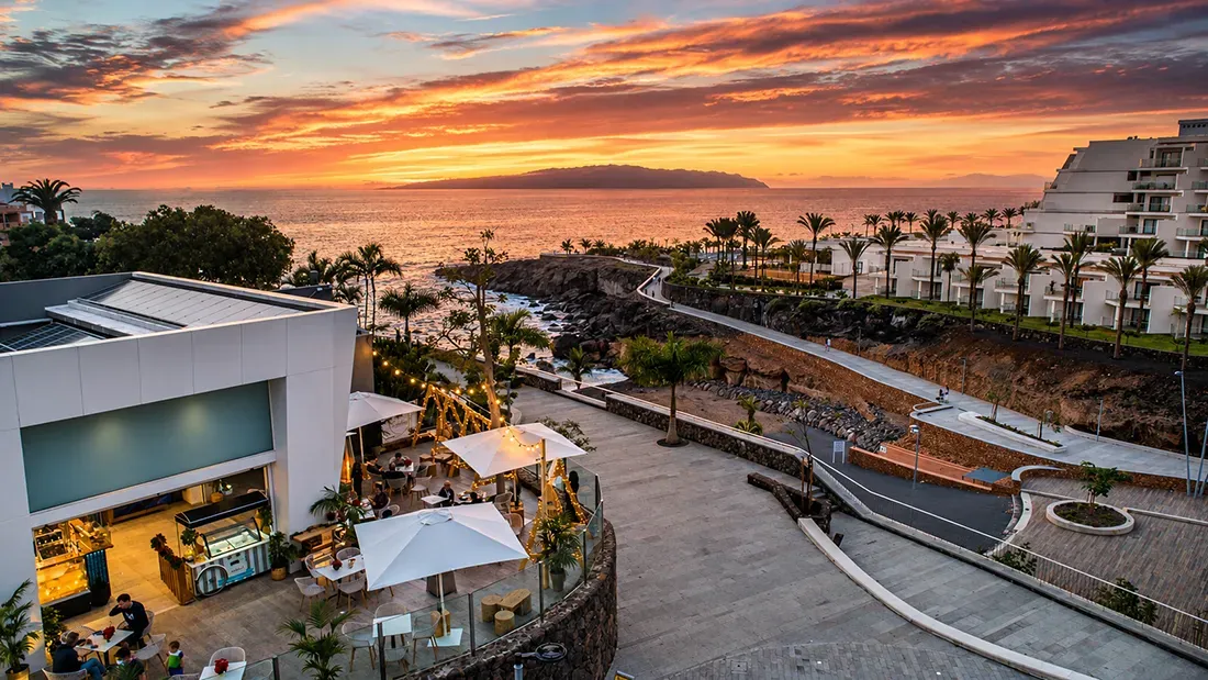 Sunset view of coastal resort with ocean, palm trees, and modern architecture