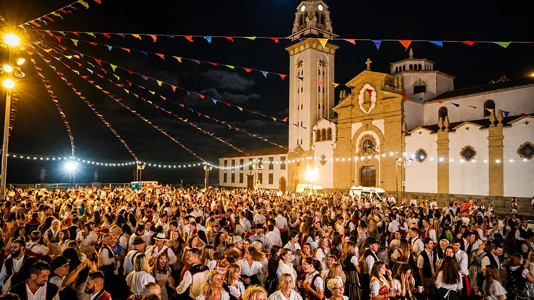 Large nighttime festival crowd gathered before illuminated church with colorful bunting