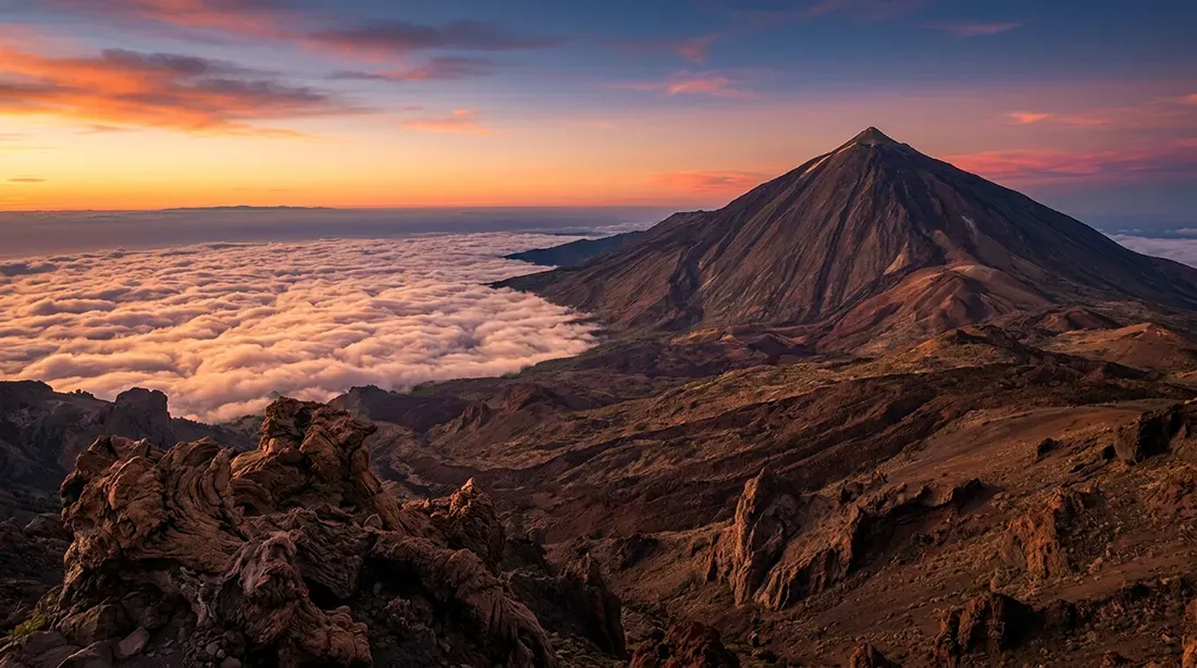 Volcanic mountain peak rises above sea of clouds at sunset