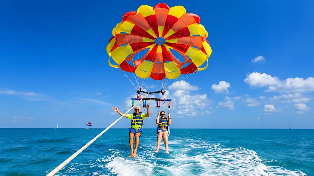 Two people parasailing behind boat in turquoise ocean