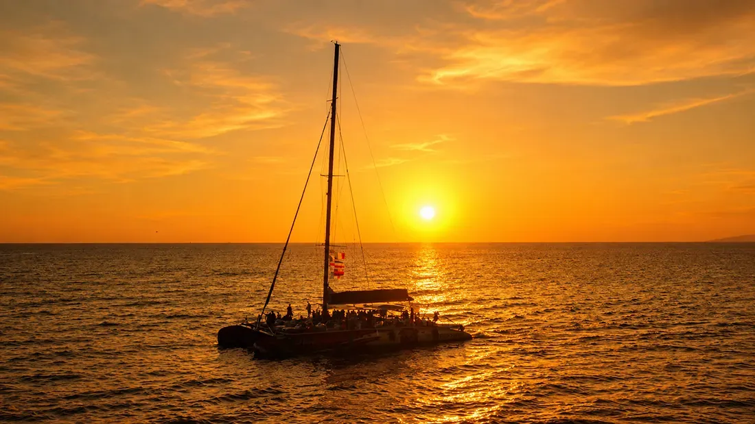 Catamaran with passengers sailing toward golden sunset over ocean
