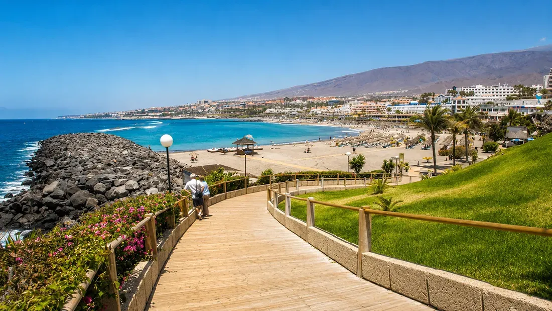 Wooden boardwalk overlooking Tenerife beach with turquoise waters and resorts