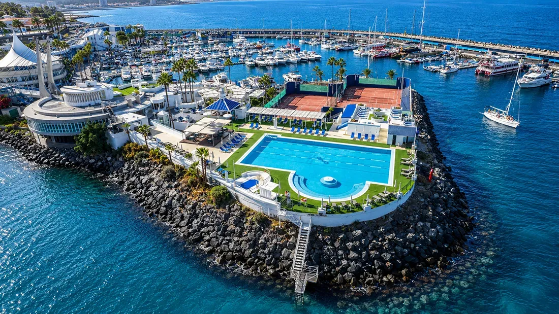 Aerial view of marina with swimming pool, tennis court, and moored sailboats
