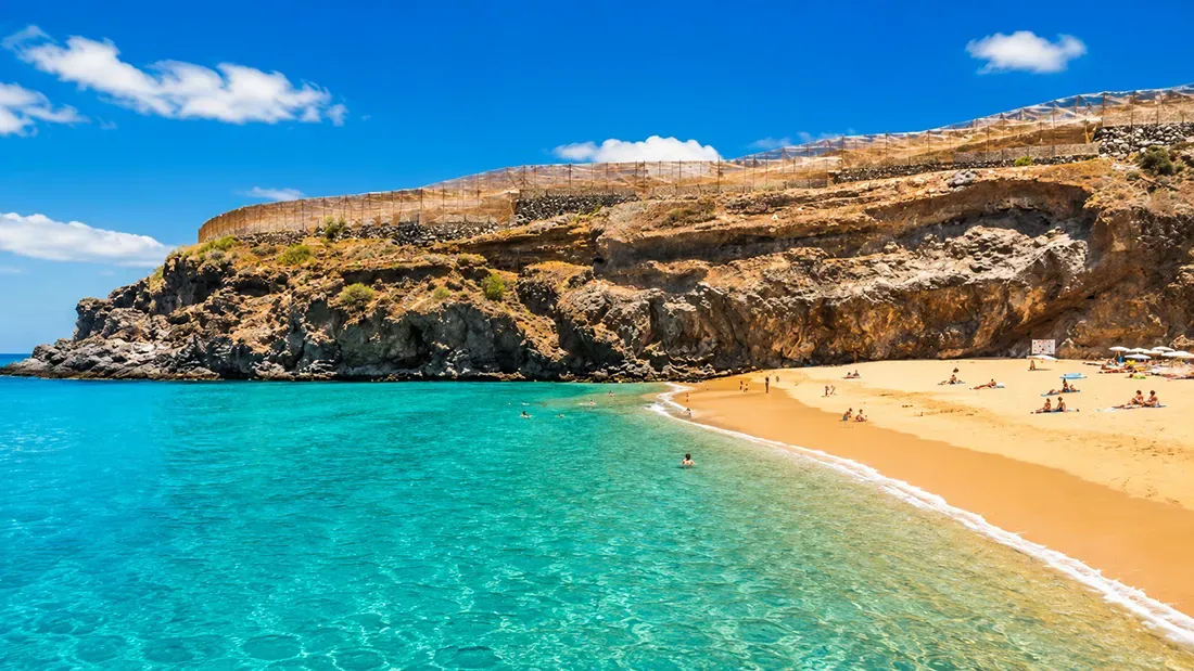 Golden beach cove with turquoise water and rocky cliffs, swimmers enjoying