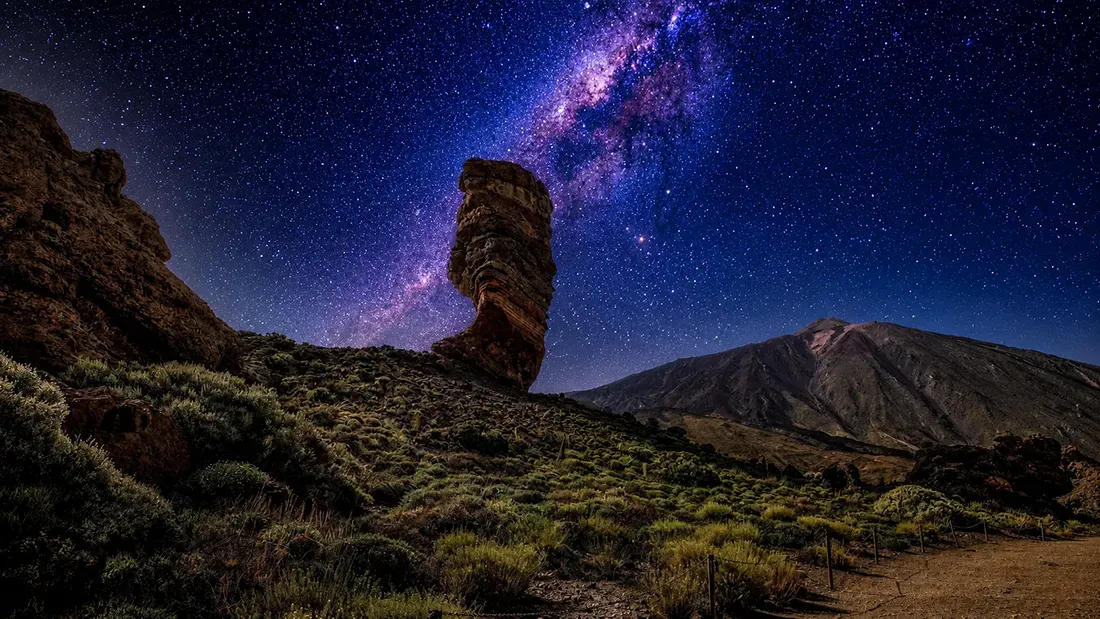 Milky Way galaxy above volcanic rock formation and mountain landscape at night