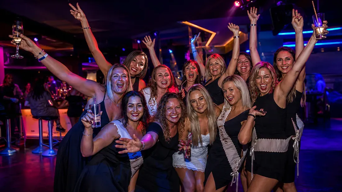 Large group of women celebrating and dancing in nightclub with colorful lighting