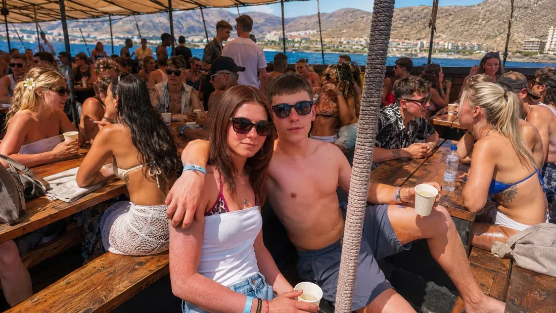 Guests enjoying drinks at wooden tables under canopy on boat party