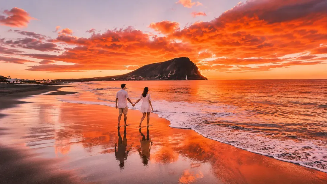 Couple holding hands wading in ocean at sunset with island mountain backdrop