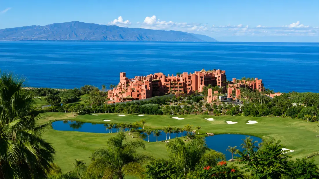 Coastal golf course with terracotta buildings overlooking ocean and mountains