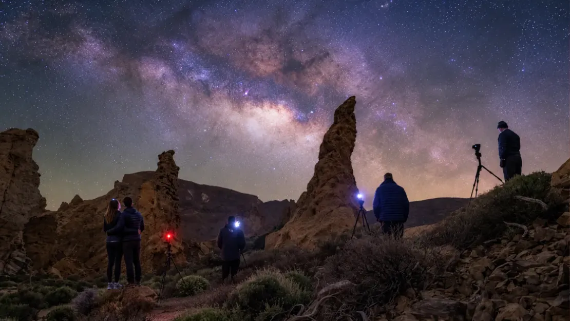 Stargazers photographing Milky Way above desert rock formations at night