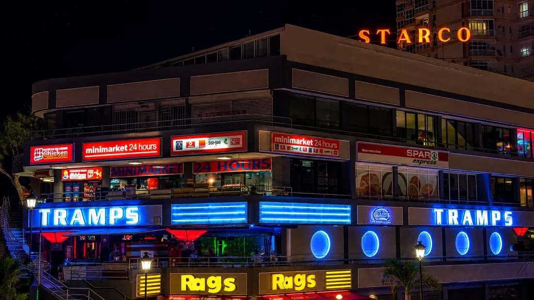 Nighttime street view of illuminated storefronts including Starco, Tramps and Rags signs