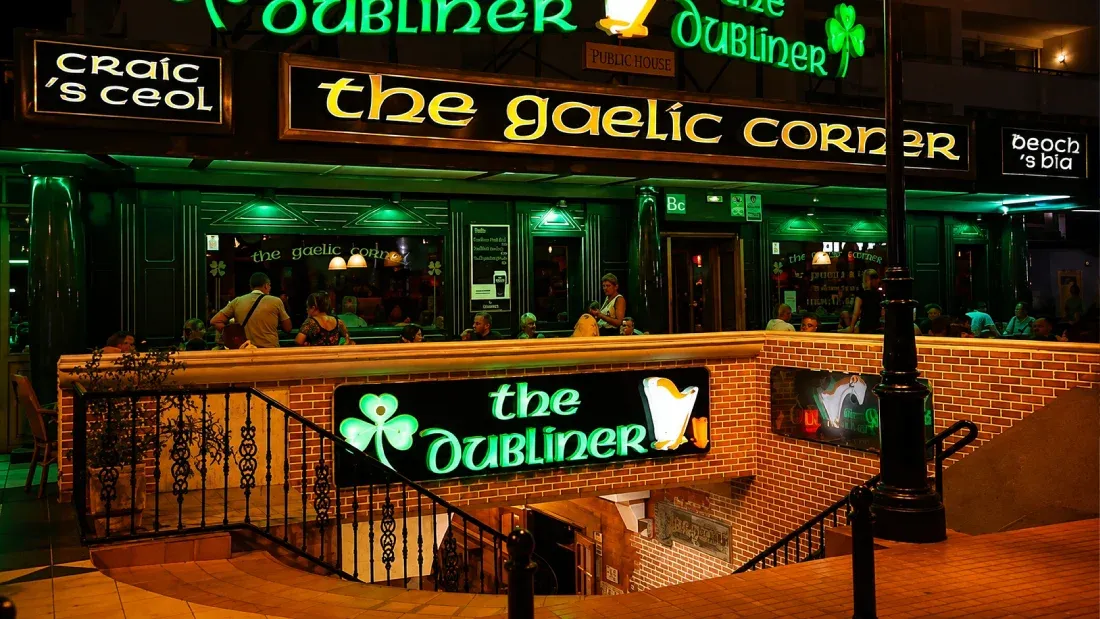 Irish pub storefront at night with green neon signage and street-level seating