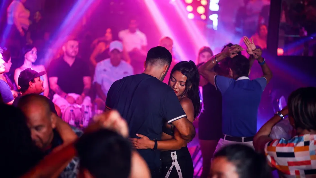 Couple dancing together on crowded nightclub dance floor with purple lighting