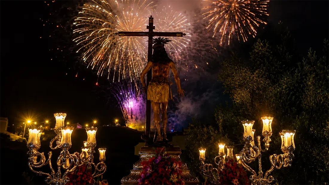 Christ statue illuminated by fireworks with golden candelabras below
